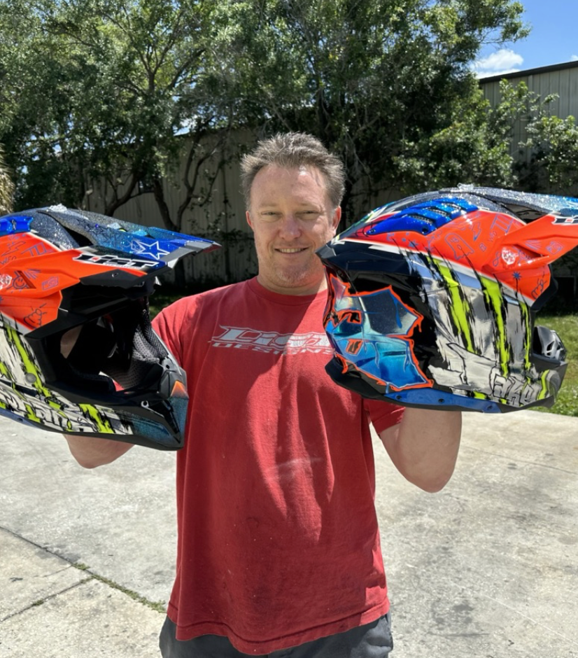 List Designs artist holding two custom-painted helmets